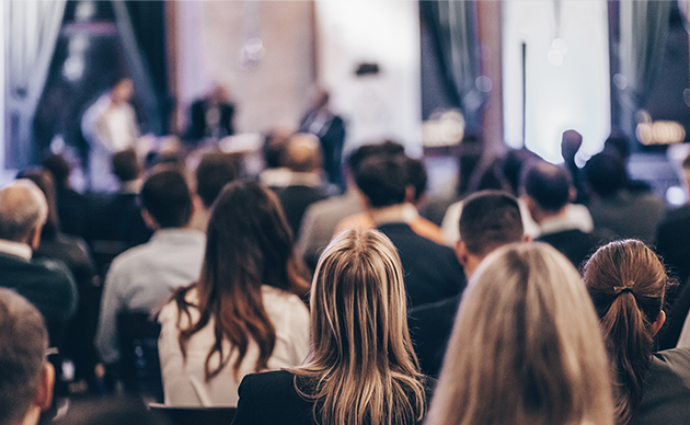 salle avec public assis devant une scène avec intervenants